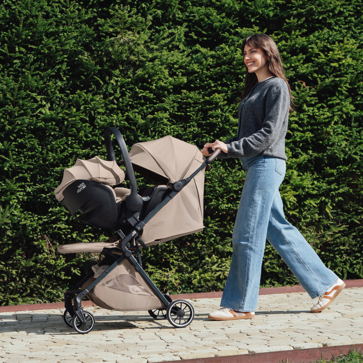 Die Mutter schiebt das Britax Römer TIRA Travel System mit Babyschale im Freien